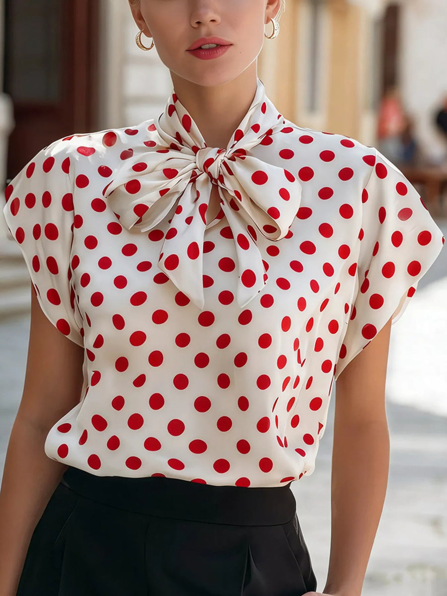 Woman wearing a red and white polka dot blouse with a bow neckline.