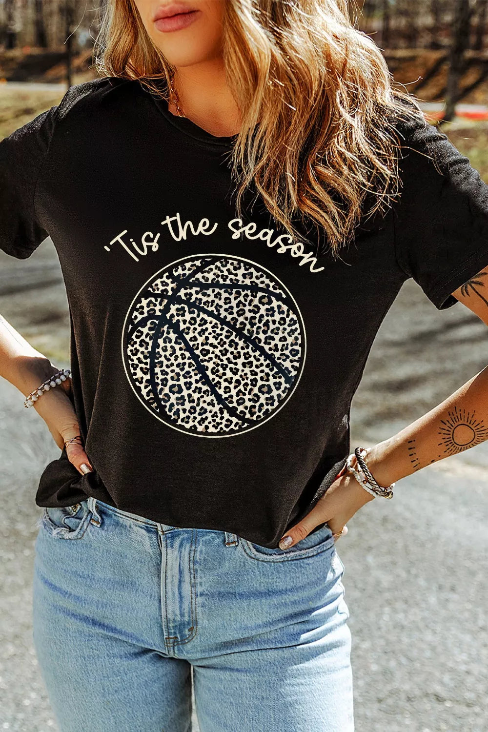 Person wearing a black t-shirt with a leopard print design and text, standing outdoors.