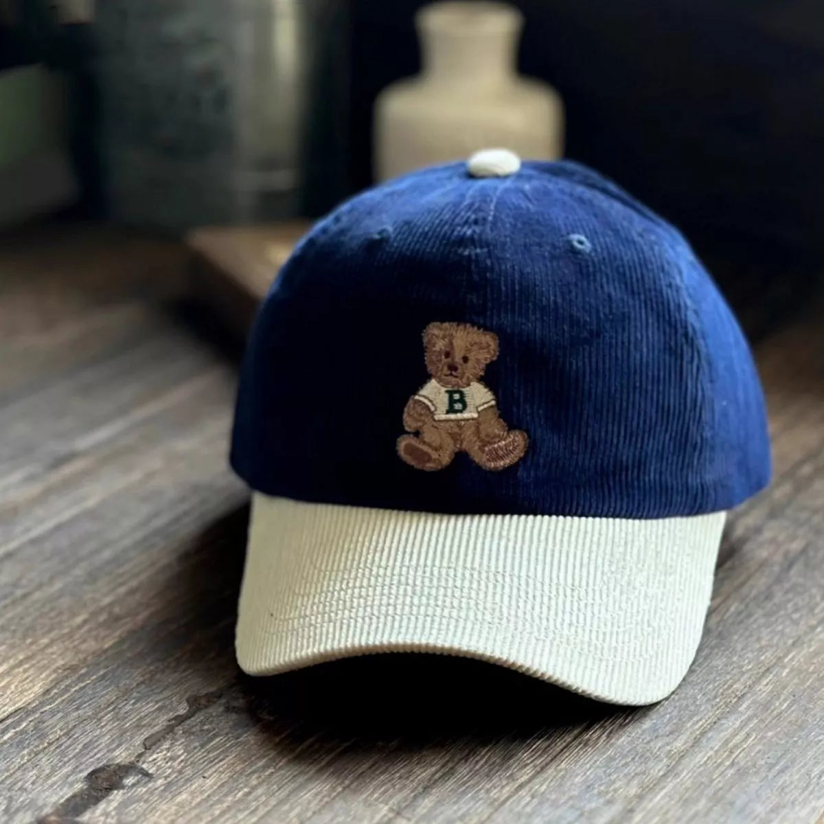 Blue and beige cap with a teddy bear emblem on a wooden surface