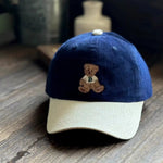 Blue and beige cap with a teddy bear emblem on a wooden surface