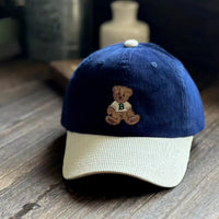Blue and beige cap with a teddy bear emblem on a wooden surface