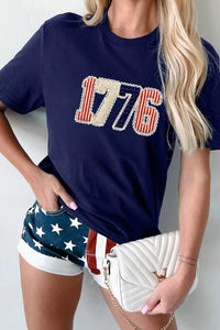 Person wearing a navy blue t-shirt with '1776' design, American flag shorts, and white handbag.