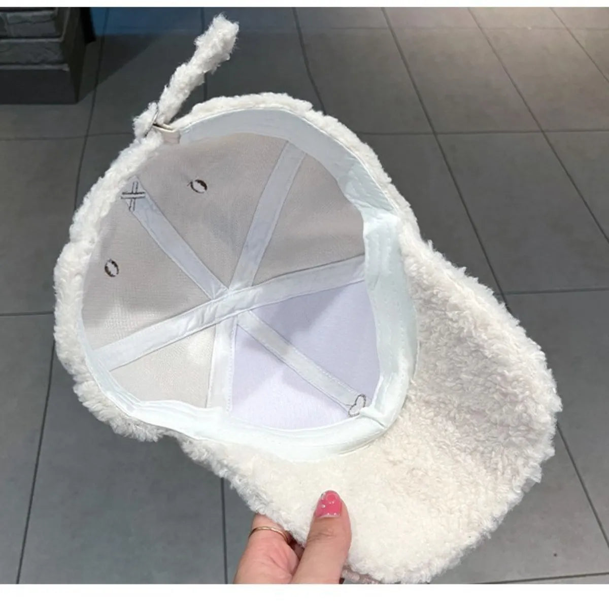 White fluffy cap held by a hand on a tiled floor