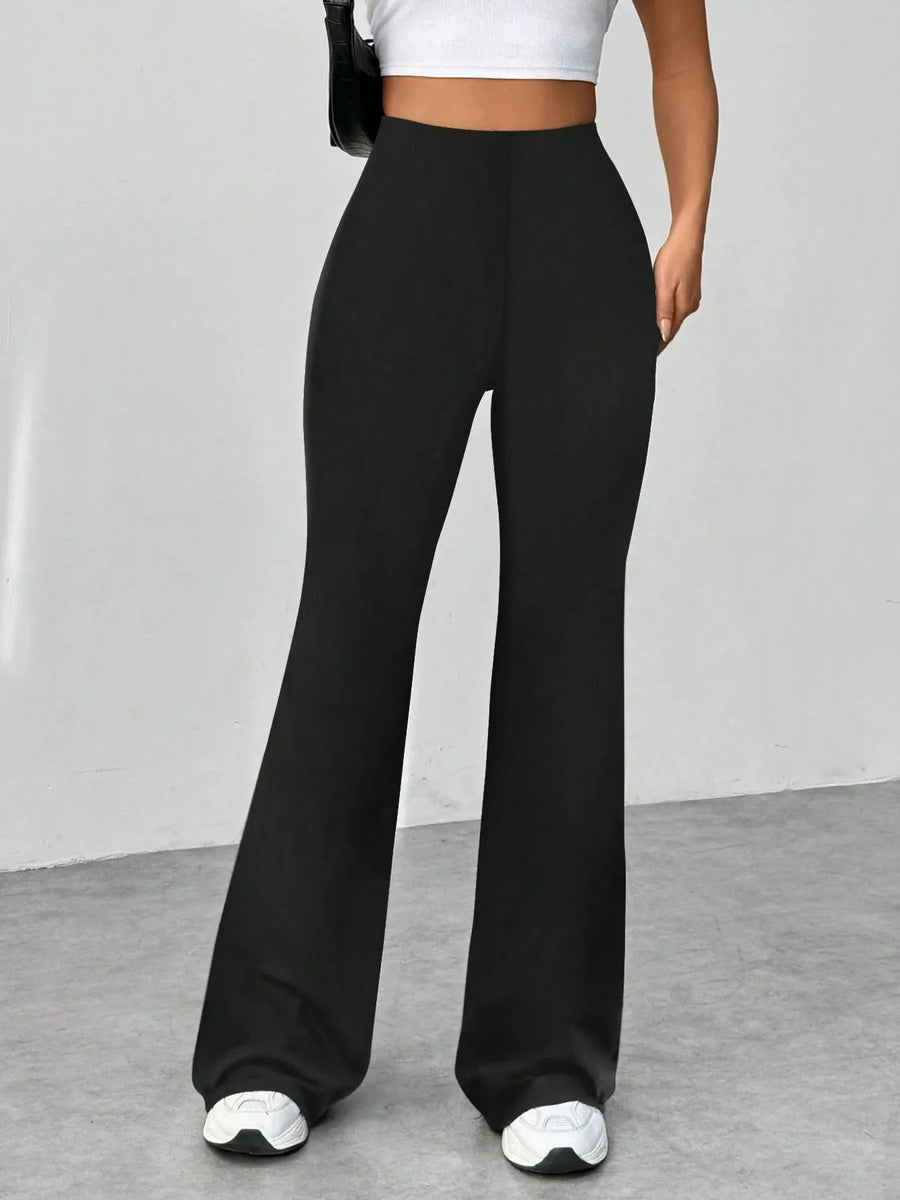 Person wearing black wide-leg pants with white sneakers on a gray floor.