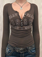 Brown long-sleeve shirt with text and jeans on a neutral background