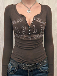 Brown long-sleeve shirt with text and jeans on a neutral background