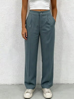 Person wearing teal pants and white sneakers against a textured white wall.