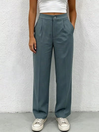 Person wearing teal pants and white sneakers against a textured white wall.