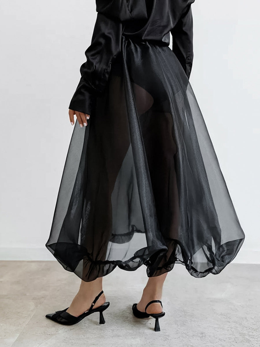Person wearing a black outfit with a sheer black skirt against a white background