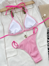 Pink bikini set on a white surface with a wooden hanger.