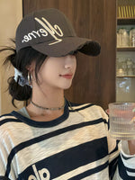 Person wearing a black cap with gold text and a striped shirt indoors.