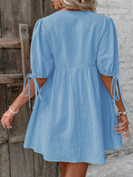 Woman wearing a blue dress with puff sleeves against a wooden and stone wall.