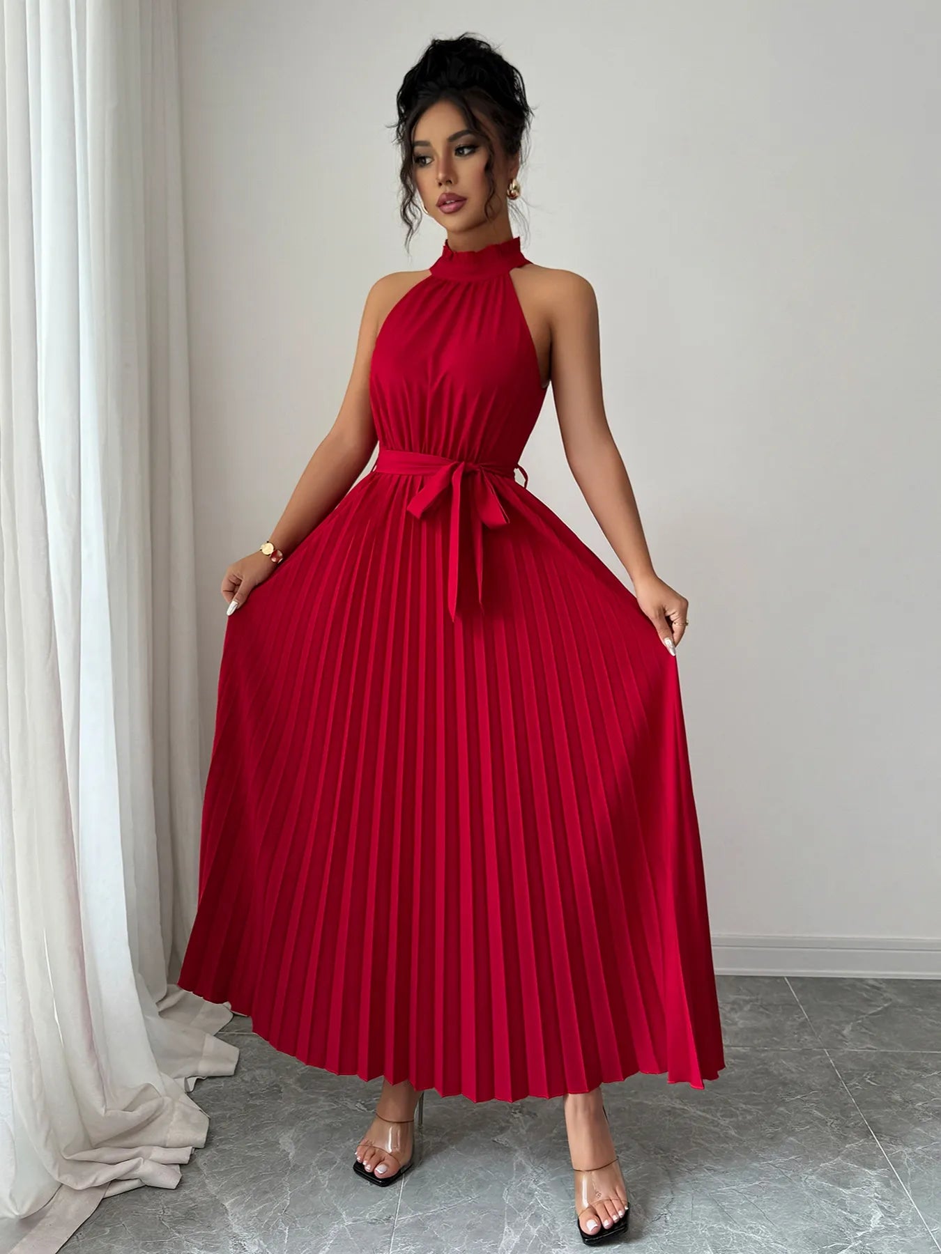 Woman wearing a red pleated dress standing against a neutral background