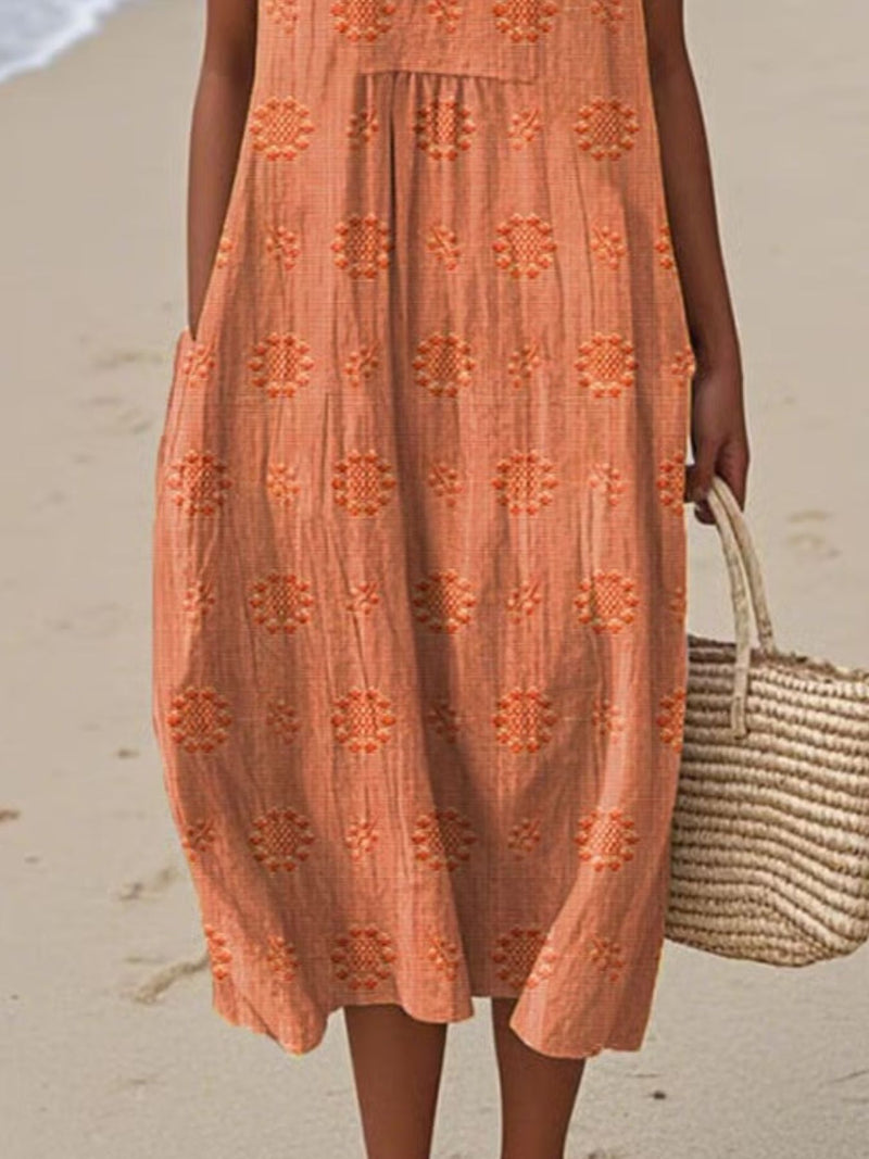 Person wearing an orange dress with a floral pattern on a beach.
