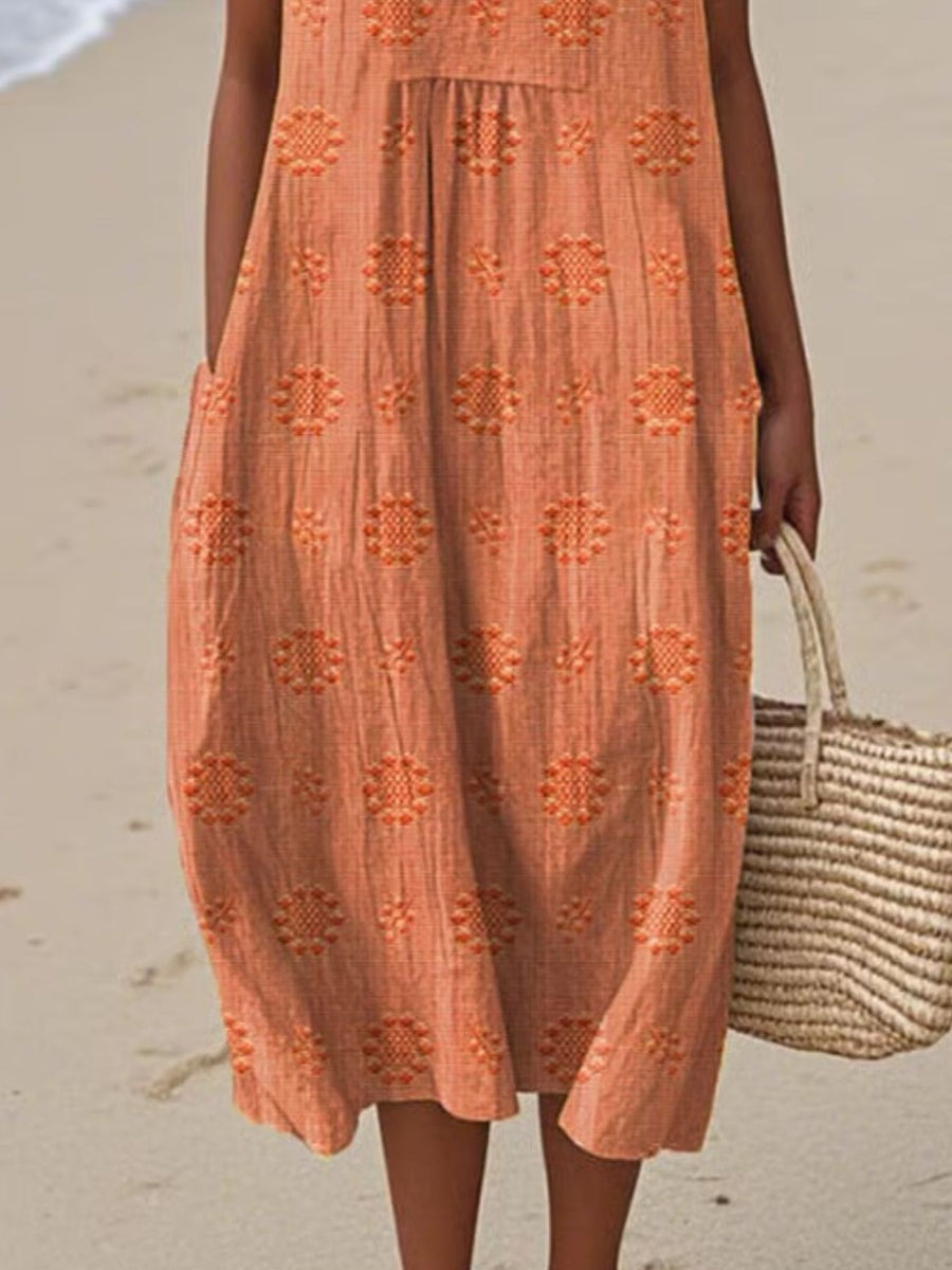 Person wearing an orange dress with a floral pattern on a beach.