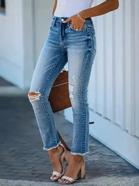 Person wearing ripped blue jeans and high-heeled sandals, holding a brown clutch.