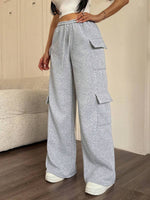 Person wearing gray cargo pants standing in a room with wooden flooring and a beige wall.
