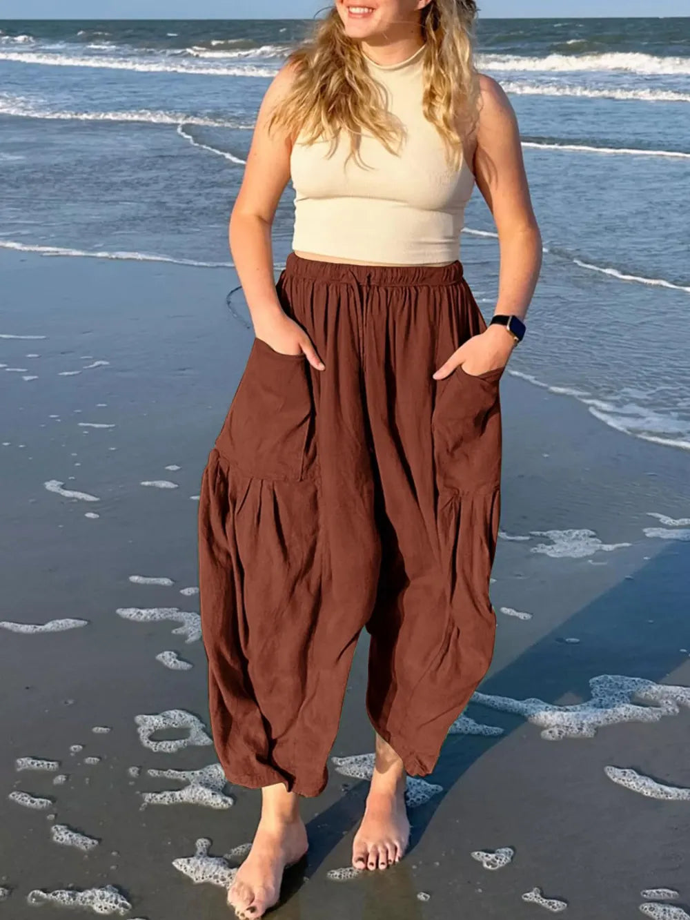 Woman wearing a beige top and brown harem pants standing on a beach.