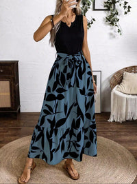 Woman wearing a black sleeveless top and blue leaf-patterned skirt indoors.
