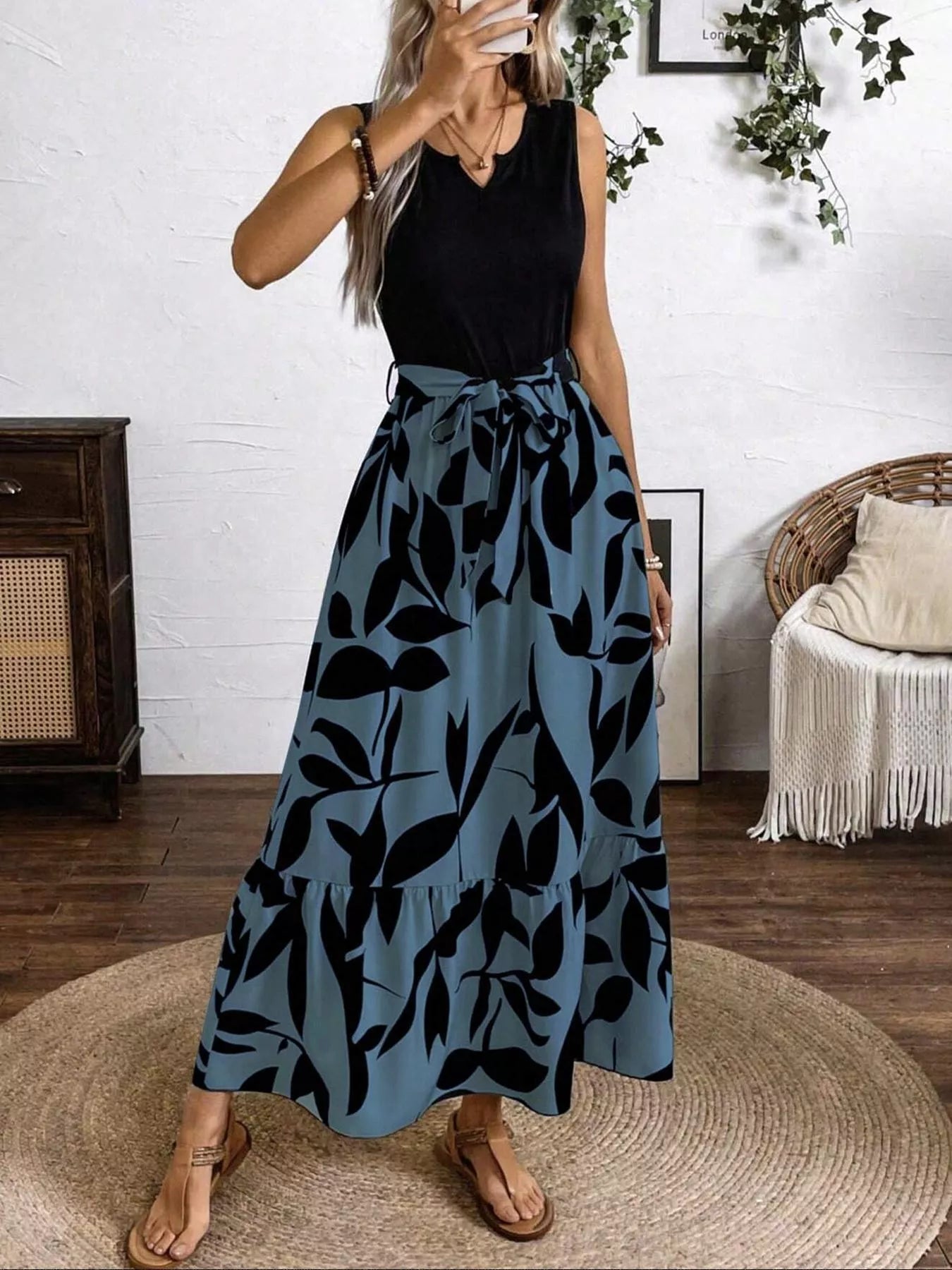 Woman wearing a black sleeveless top and blue leaf-patterned skirt indoors.