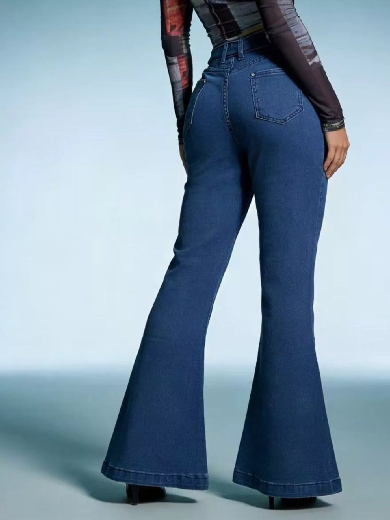 Person wearing blue flared jeans on a light blue background