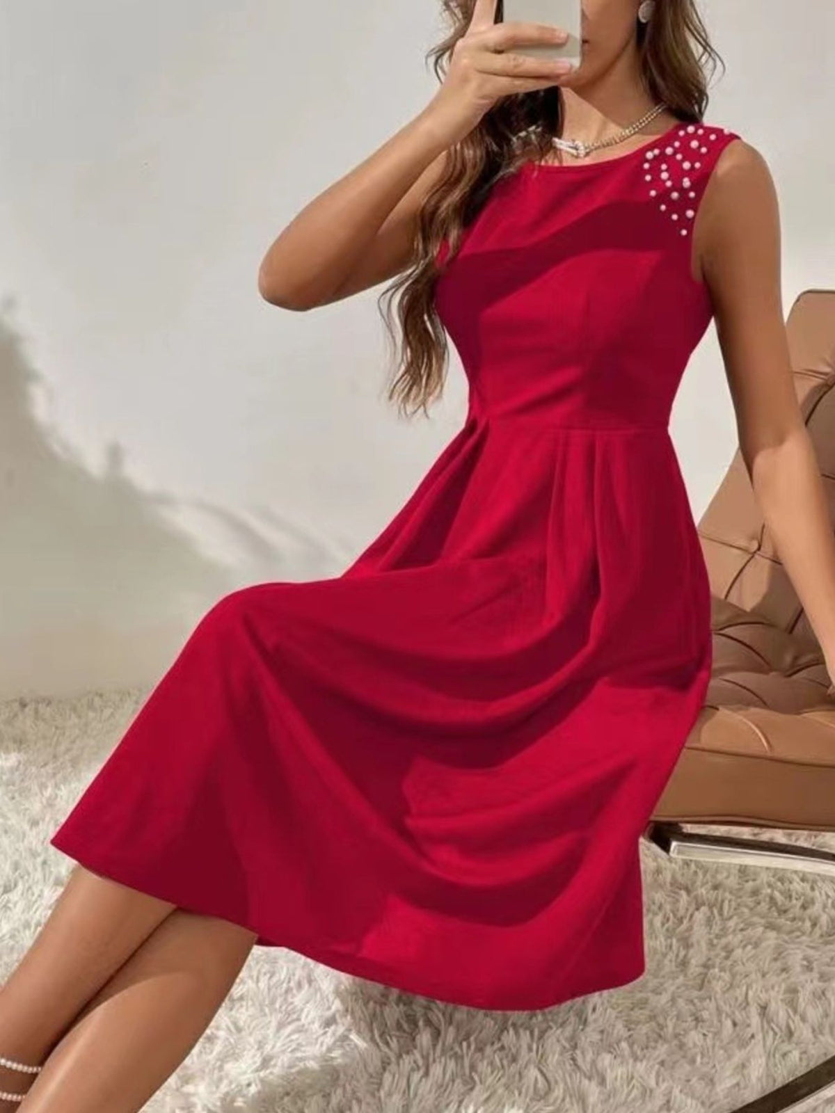 Red dress with pearl embellishments worn by a person, sitting on a textured surface.
