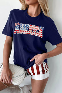 Person wearing a navy blue t-shirt with 'AMERICA' printed in red and white, holding a white handbag.