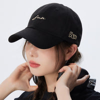 Person wearing a black cap with gold embroidery on a white background