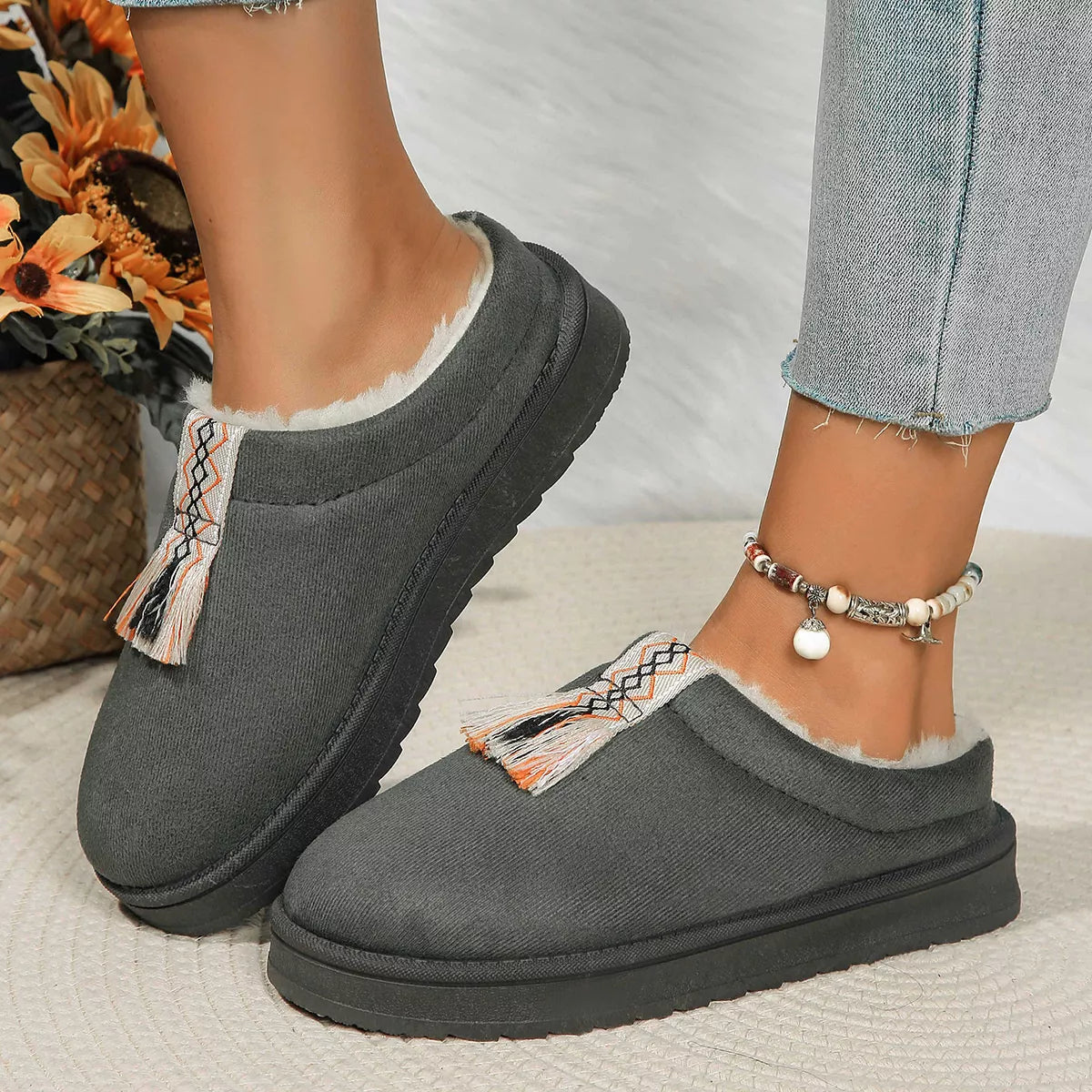 Gray slippers with decorative tassels worn by a person on a light background