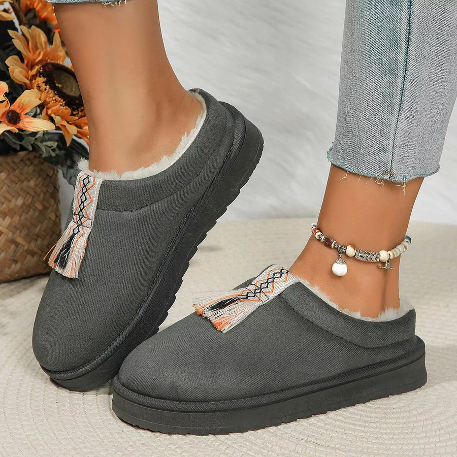 Gray slippers with decorative tassels worn by a person on a light background