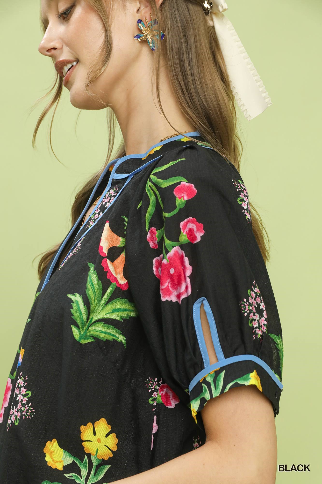 Woman wearing a black top with colorful floral embroidery on a light green background