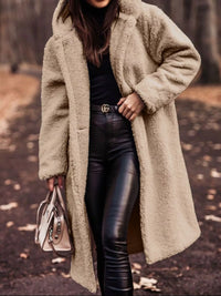 Person wearing a beige teddy coat and black leather pants, holding a beige handbag.