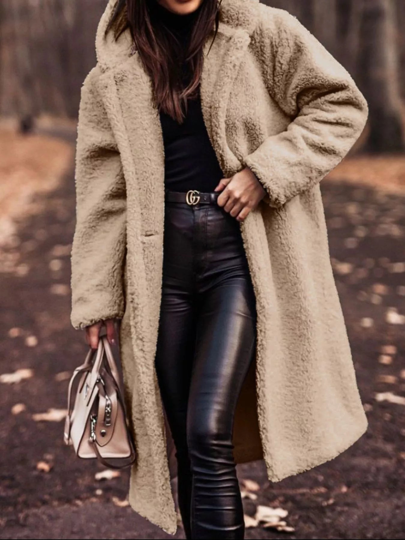 Person wearing a beige teddy coat and black leather pants, holding a beige handbag.