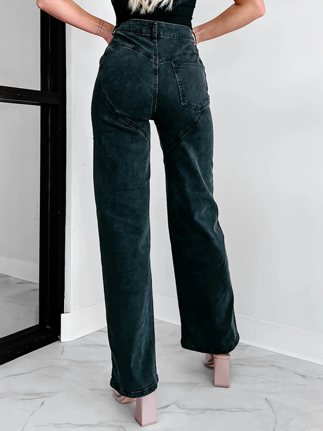 Person wearing dark green wide-leg jeans standing against a white wall.