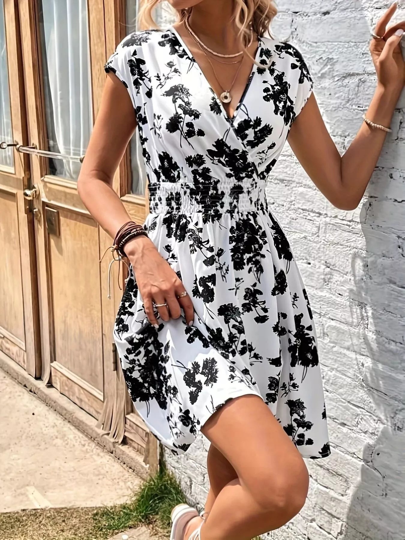 Woman wearing a black and white floral dress against a white wall.