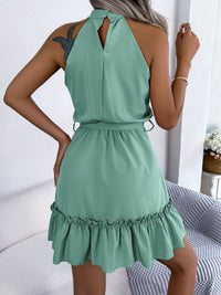 Woman wearing a green halter neck dress with ruffled hem in a minimal indoor setting.