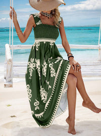 Woman in a green dress with white patterns sitting on a swing by the ocean.