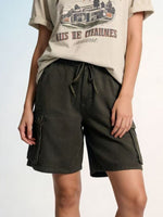 Person wearing dark cargo shorts and a beige t-shirt with graphic design on a light gray background