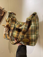 Plaid handbag with a small plush toy attached, held against a neutral background.