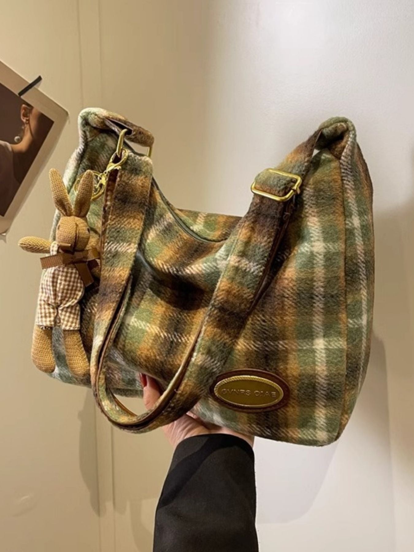 Plaid handbag with a small plush toy attached, held against a neutral background.