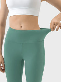 Person wearing green leggings and a white sports bra on a light gray background