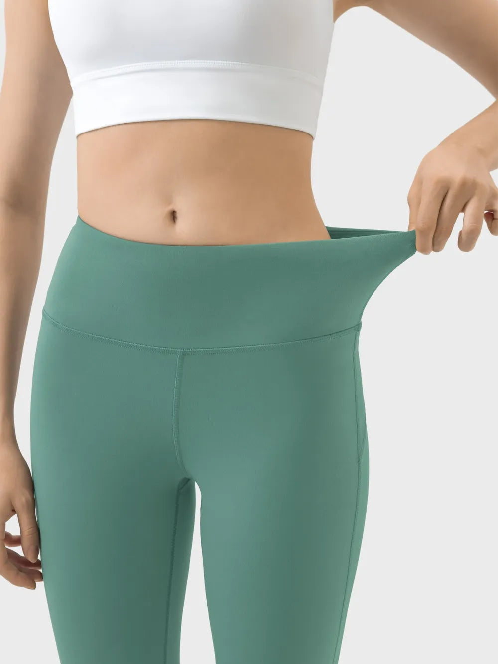 Person wearing green leggings and a white sports bra on a light gray background