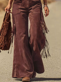 Brown suede pants with fringe details worn by a person, holding a matching brown fringed bag.
