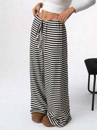 Black and white striped wide-leg pants worn by a person on a white background