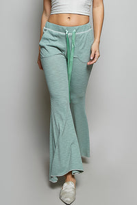Person wearing teal flared pants with a white top on a plain background