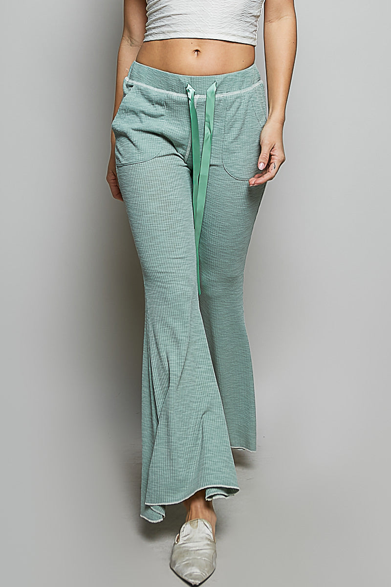 Person wearing teal flared pants with a white top on a plain background