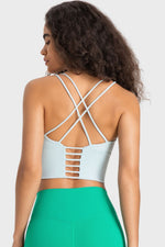 Person wearing a light blue sports bra with criss-cross back design and green leggings on a plain background