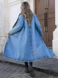 Person wearing a long denim coat walking on a street.
