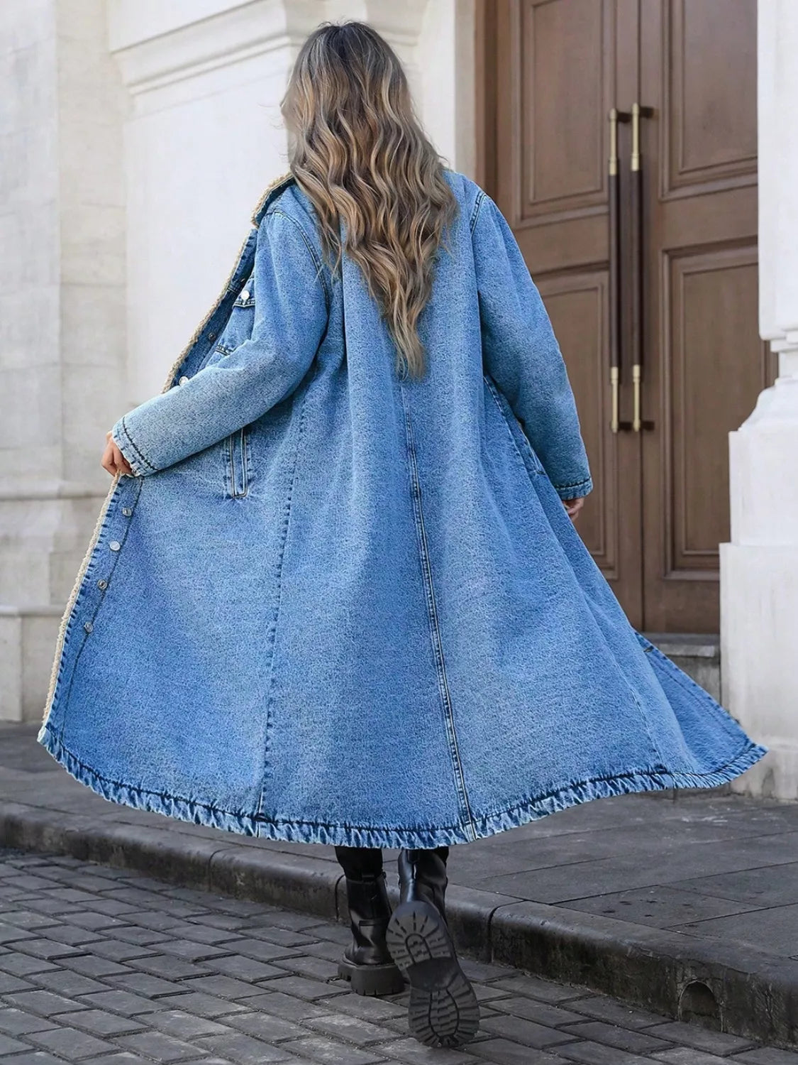 Person wearing a long denim coat walking on a street.