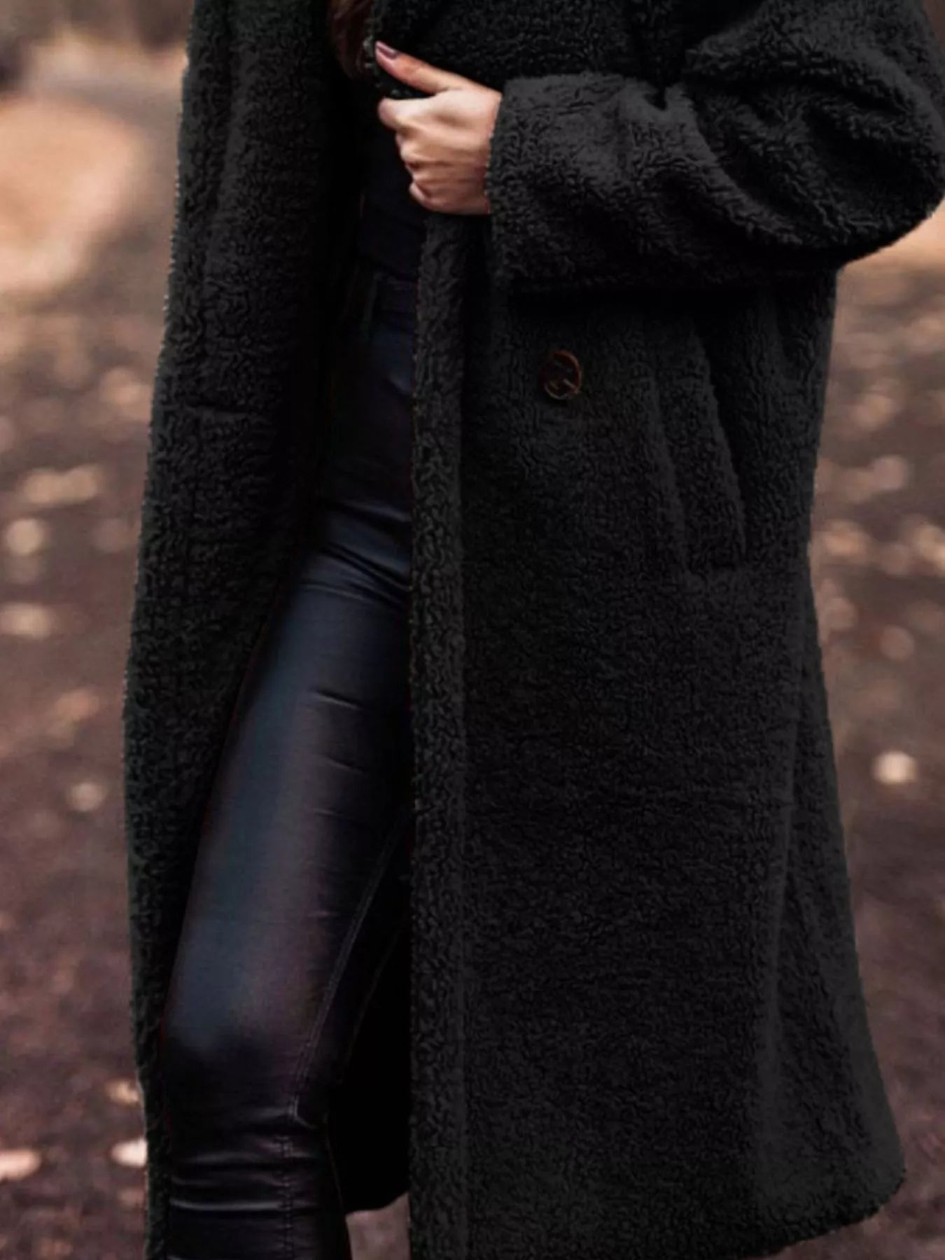 Person wearing a long black coat with a blurred background
